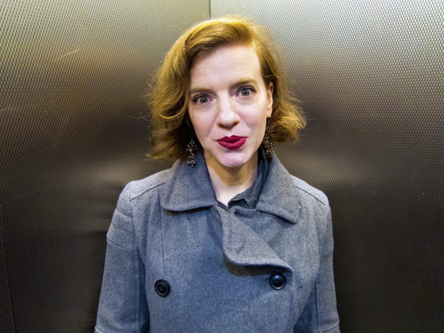 Mary in an Elevator Wearing a Gray Coat with a Yellow Light and Funny Face