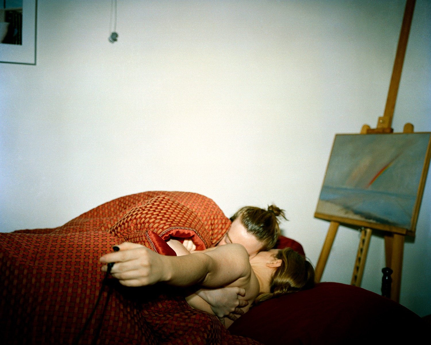 Photographer in Image Hugging Girlfriend in Bed, Rainbow Painting Behind Them